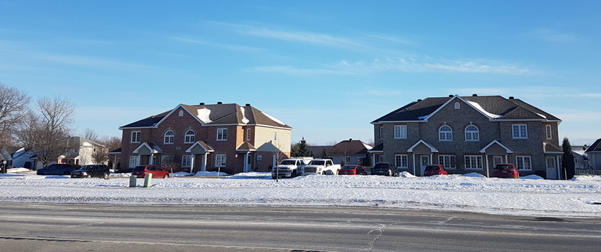 Newer fourplexes on the boundary of a newer subdivision of semi-detached and detached homes. As is often the case, multi-unit housing is used as a buffer in between busy roads and detached and semi-detached houses. Note the abundance of parking in an auto-oriented part of the City.
