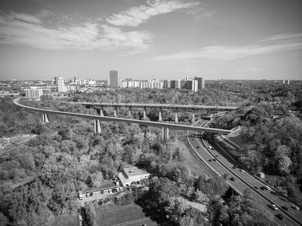 Artist's rendering of the future Ontario Line crossing the Don Valley. The Ontario Line will emerge from a tunnel (right) under Minton Place in East York, then cross the Don Valley on a 500-metre-long bridge designed by American engineering firm HDR. Illustration shows the existing Millwood Overpass Bridge in the background. The rail bridge will carry two tracks and be supported by just three twinned piers using a balanced segmental construction method. The longest span between piers is 137 metres. The artist has depicted mature trees in the Don Valley. In fact, it will take some 50 years for the tree canopy to recover from the extensive clearcutting (Image credit: Metrolinx).