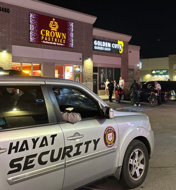 Groups hanging out by their cars and bikes at Ridgeway Plaza. Night shift security drives by.